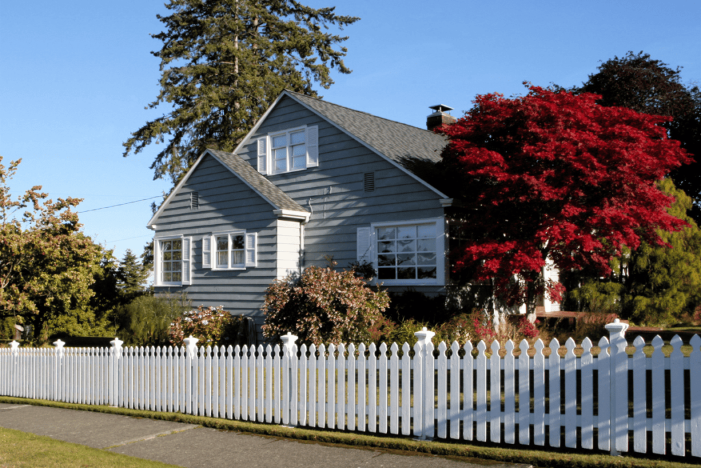 Gray siding on a house with white window shutters and a white picket fence lining the property